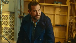 Noah Wyle wears a blue coat and denim shirt